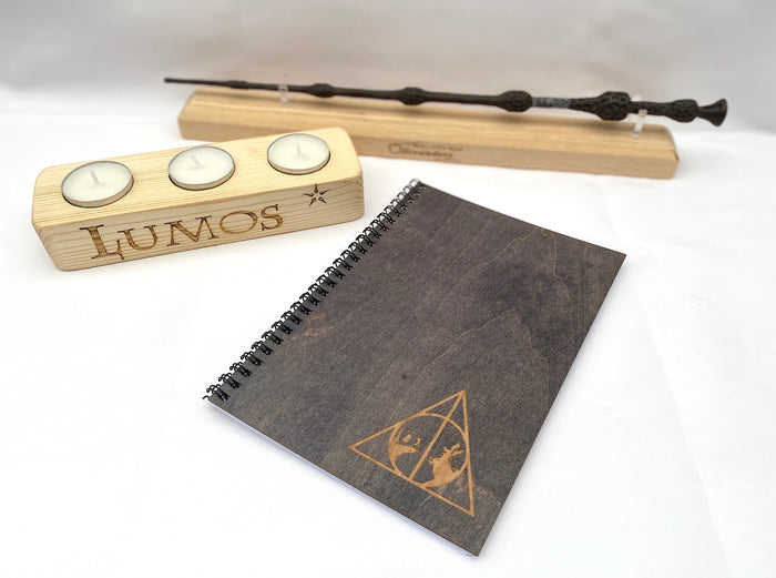 Wooden wand, tea light holder with 'Lumos' engraving, and notebook with engraved design on a white background