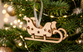 A wooden sleigh Christmas ornament hanging from a green Christmas tree with warm white string lights and gold bokeh background lights.