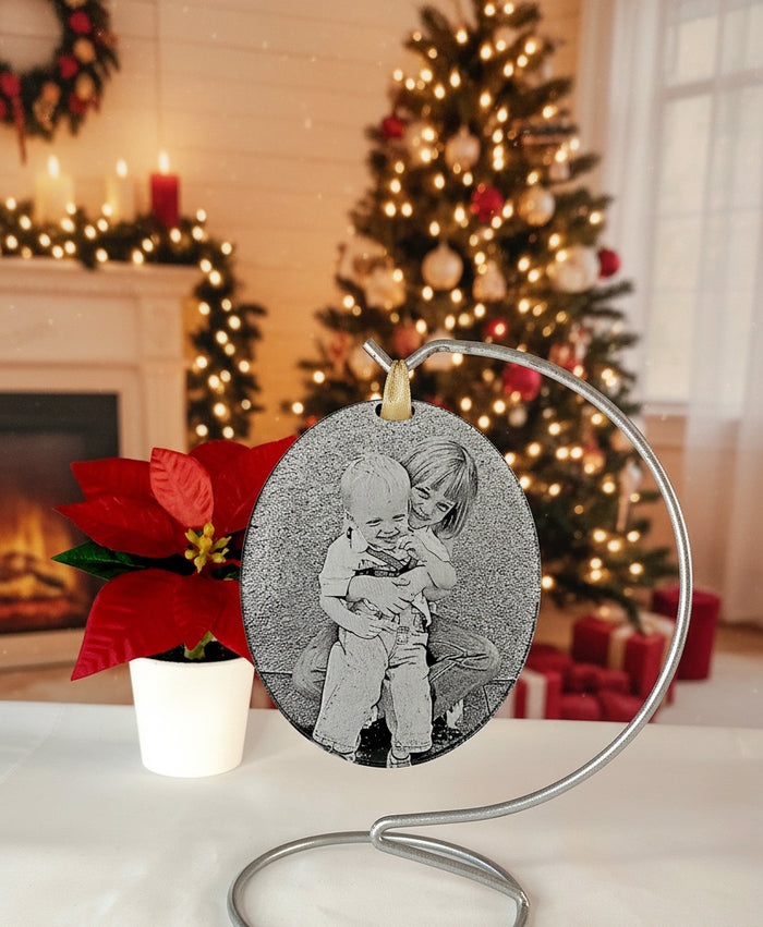 Personalised photo Christmas tree decoration with a decorated and lit tree blurred behind.