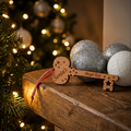 A wooden Santa's Magic Key ornament engraved with 'Santa's Magic Key' and stars, hanging from a red ribbon, resting on a wooden mantelpiece next to a blurred Christmas tree and silver ornaments.