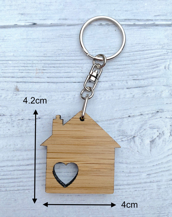 House-shaped keychain with a heart cutout and measurements on a light wooden background