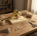 A mini hot glue gun resting on a custom made wooden stand, with decorative green leaves on the left and woven ball ornaments on the right, all on a white background.